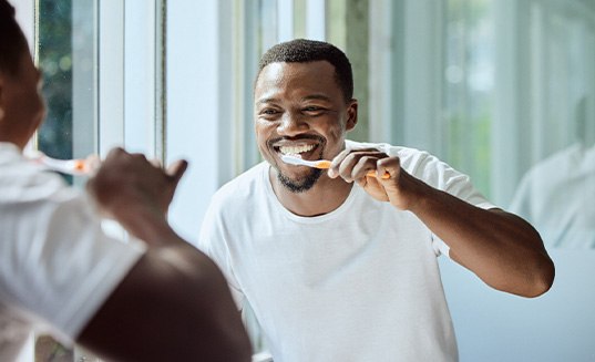 Man smiling while brushing his teeth