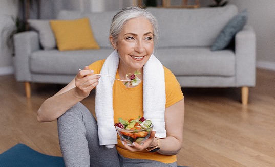 Senior woman smiling while eating salad at home