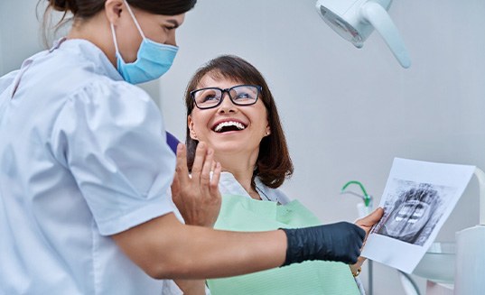 Woman smiling with dentist while reviewing X-ray