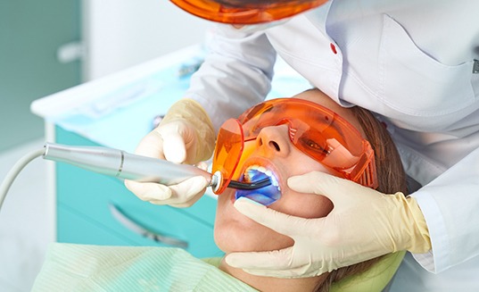 Dentist leaning over patient to apply UV light to back teeth