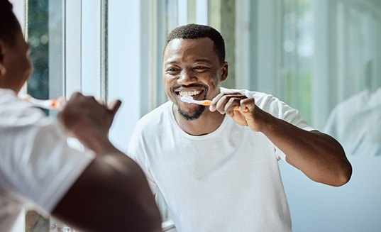 Man smiling while brushing his teeth